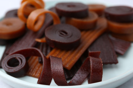 Tasty fruit leather rolls on white table, closeup