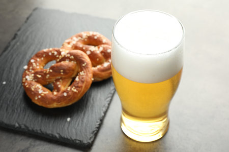 Tasty pretzels and glass of beer on dark textured table, closeup