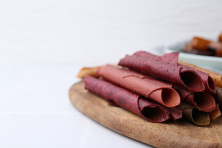 Tasty fruit leather rolls on white tiled table, closeup. Space for textの写真素材