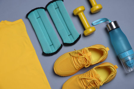 Sportswear, ankle weights, water bottle and dumbbells on grey background, flat lay