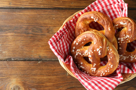 Tasty pretzels with salt in wicker basket on wooden table, top view. Space for textの写真素材
