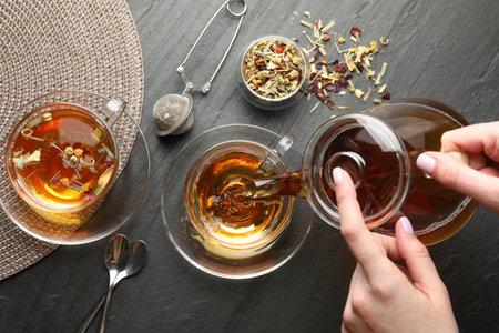 Woman pouring herbal tea from teapot into cup at black table, top viewの写真素材