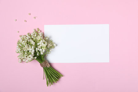 Beautiful lily-of-the-valley flowers and blank card on light pink background, top view. Space for textの写真素材
