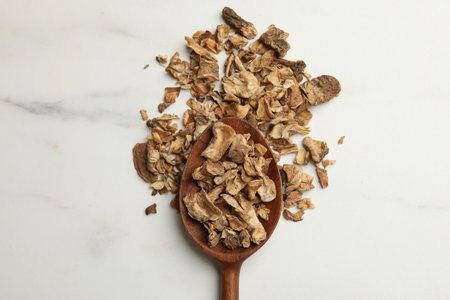 Pieces of dry chicory roots in spoon on white table, top view