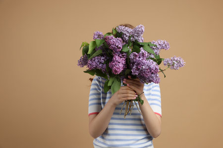 Teenage girl hiding behind bouquet of lilac flowers on beige backgroundの写真素材