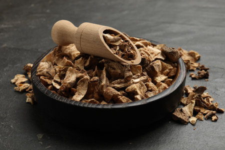 Pieces of dry chicory roots in bowl and scoop on dark textured table, closeupの写真素材