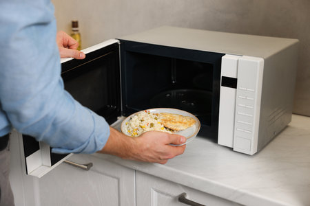 Man putting plate with lunch into microwave in kitchen, closeupの写真素材