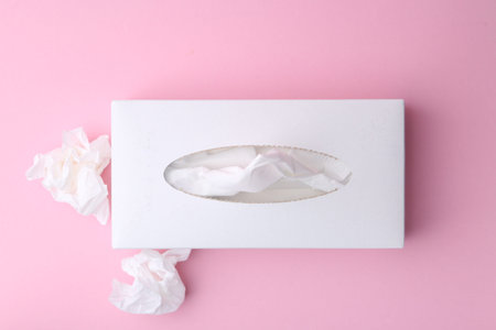 Box with paper handkerchiefs and crumpled tissues on pink background, flat lay