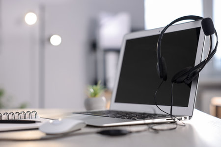 Headset with microphone, laptop and planner on white wooden desk in office, closeup. Space for textの写真素材