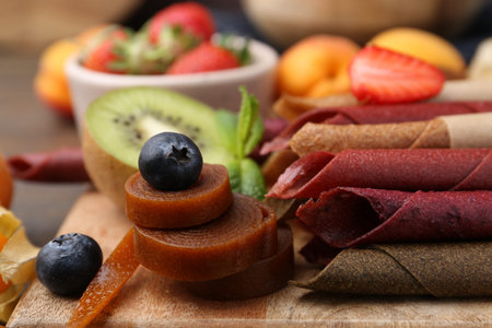 Tasty candied leather rolls, fruits and berries on wooden table, closeup