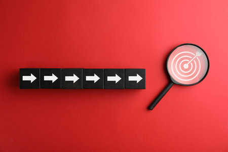 Targeting. Cubes with arrows pointing at magnifying glass with bullseye inside on red background, top viewの写真素材