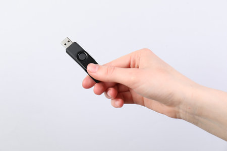 Hand with modern flash drive on light grey background, closeup