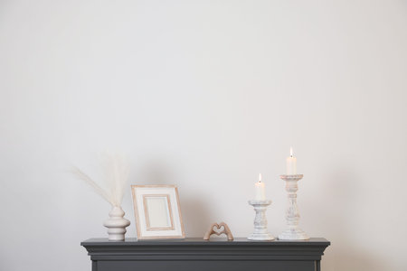 Stylish candlesticks with burning candles and other decor on fireplace near white wall indoorsの写真素材