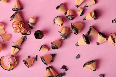 Shavings of pencils on light pink background, flat lay