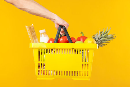 Man holding shopping basket with different products on yellow background, closeupの写真素材