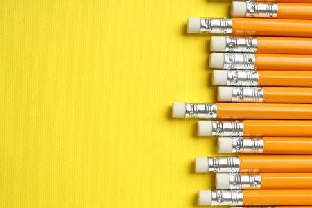 Pencils with erasers on yellow background, flat lay. Space for textの写真素材