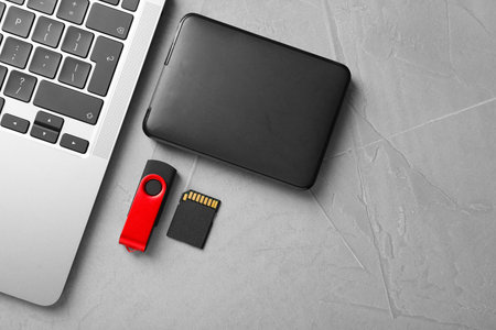 Flash drive, SD memory card, external hard disk and laptop on light grey table, flat lay. Space for...