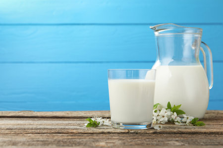Fresh milk and blossoms on wooden table against light blue background. Space for textの写真素材