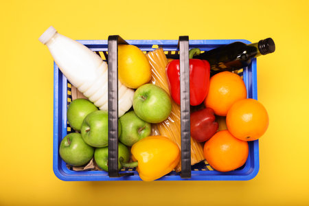 Plastic shopping basket full of products on yellow background, top viewの写真素材