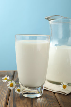 Fresh milk and flowers on wooden table against light blue background, closeupの写真素材