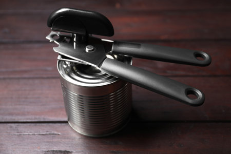 Can opener and tin on wooden table, closeup