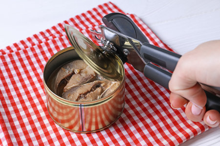 Woman opening tin of fish with can opener at white wooden table, closeupの写真素材