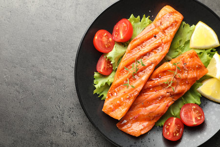 Tasty grilled salmon served with lettuce, tomatoes and lemon on grey table, top view. Space for textの写真素材