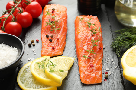Seafood. Pieces of salmon fillet, spices, tomatoes and lemon slices on table, closeup