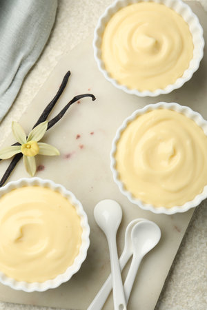 Tasty vanilla pudding with spoons, pods and flower on light textured table, flat lay