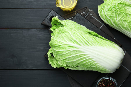 Fresh Chinese cabbages, oil and peppercorns on black wooden table, flat lay. Space for textの写真素材