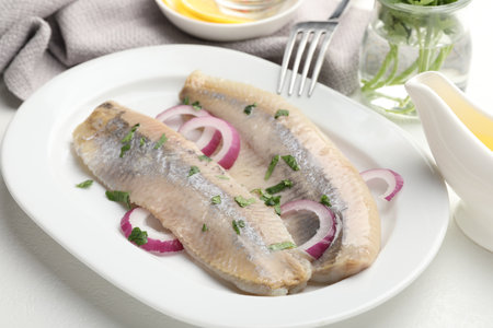 Tasty herring fillets with onions and parsley served on white table, closeupの写真素材