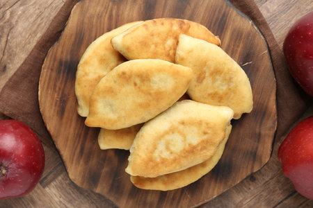Delicious fried pyrizhky (stuffed pies) and apples on wooden table, flat layの写真素材