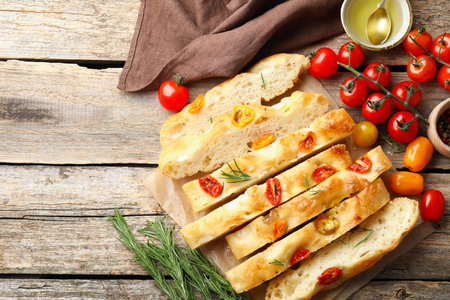 Cut delicious focaccia with tomatoes, spices and oil on wooden table, flat lay. Space for text