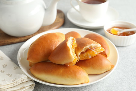 Tasty baked patties with orange jam on light grey table, closeup