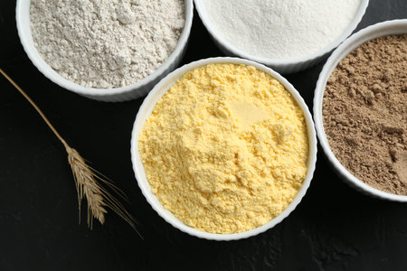 Different types of flour in bowls and spike on black table, flat layの写真素材