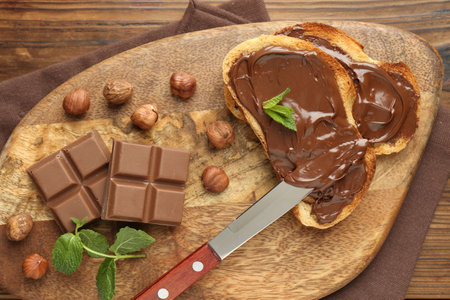 Toasts with tasty chocolate spread, pieces, mint and hazelnuts on wooden table, top viewの写真素材