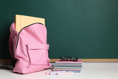 Blank green chalkboard, different stationery, backpack and glasses, space for text