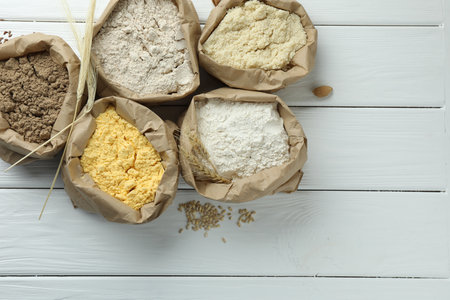 Different types of flour in paper bags on white wooden table, flat layの写真素材