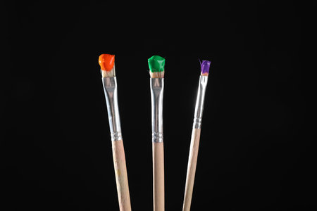 Three brushes with color paints on black background, closeupの写真素材