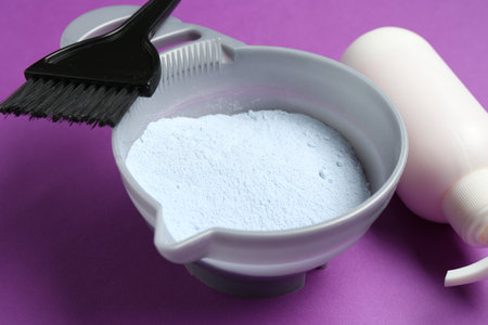 Bowl with hair bleaching powder, bottle of developer and brush on purple background, closeupの写真素材