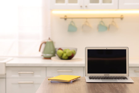 Laptop with blank screen and notebooks on wooden table in kitchen. Mockup for designの写真素材