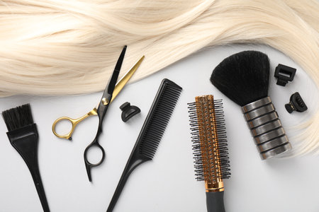 Different hairdresser's tools and blonde hair lock on light grey background, flat layの写真素材