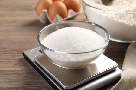 Digital kitchen scale with bowl of sugar and other products on wooden table, closeupの写真素材