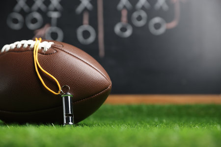 American football ball and whistle on green grass against chalkboard with game scheme, closeup. Space for textの写真素材