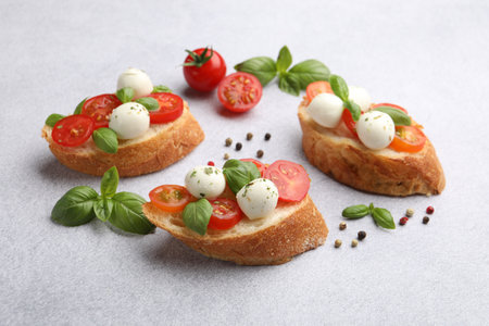 Tasty sandwiches with mozzarella cheese balls, tomato and basil on light grey tableの写真素材