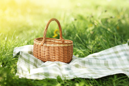 Wicker basket and blanket on green grass outdoors. Space for textの写真素材