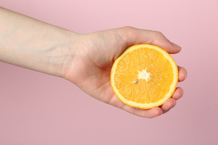 Woman with orange on pink background, closeupの写真素材