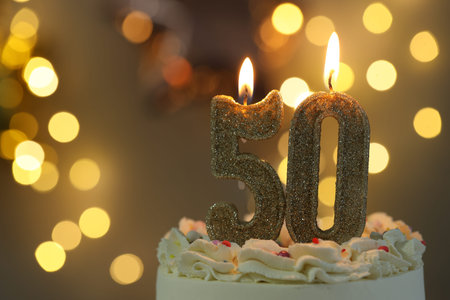 50th birthday. Burning number shaped candles on cake against blurred background with lights, closeup and space for text. Bokeh effectの写真素材