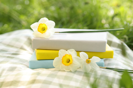 Stacked books, daffodil flowers and blanket on green grass outdoors, closeupの写真素材