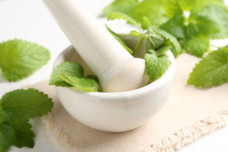 Fresh lemon balm leaves and pestle in mortar on white wooden table, closeupの写真素材